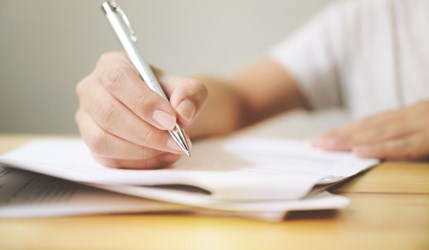 Close up of hand holding a pen poised over paperwork